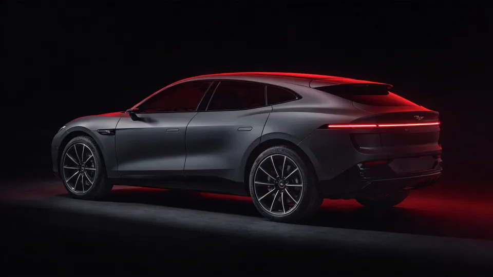 Sleek electric performance SUV with a falling coupe roofline and full-width light bar under deep red rim light